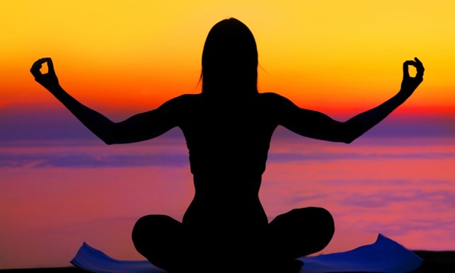 Silhouette of a person meditating practicing yoga in front of a sunset 
