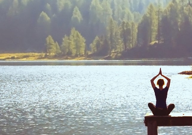 Person practicing yoga meditating outdoors in front of a lake