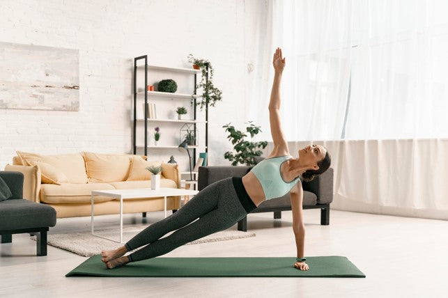 Woman in a living room holding a side plank on a green yoga mat.
